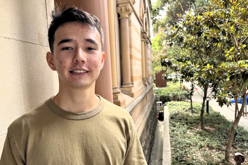 A young man stands alongside a sandstone building with window columns