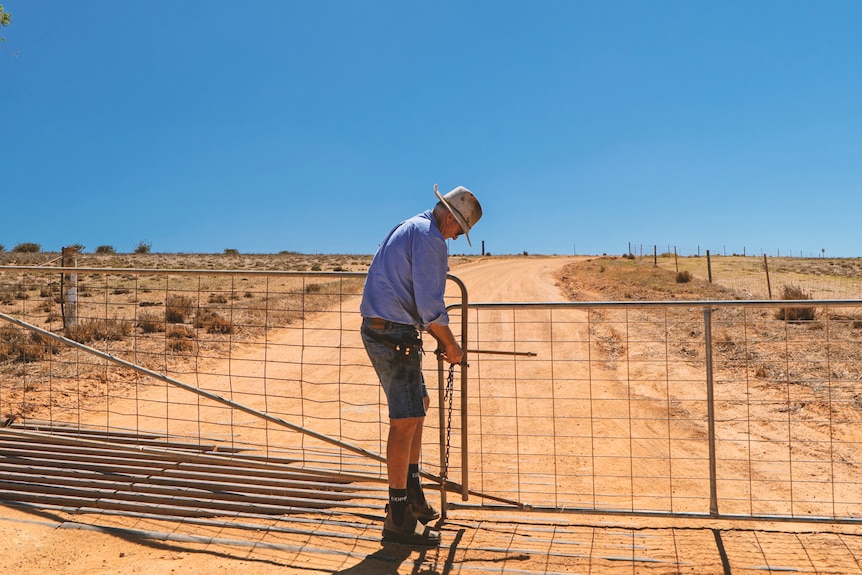 A wide shot of a man leaning over a gate locking it