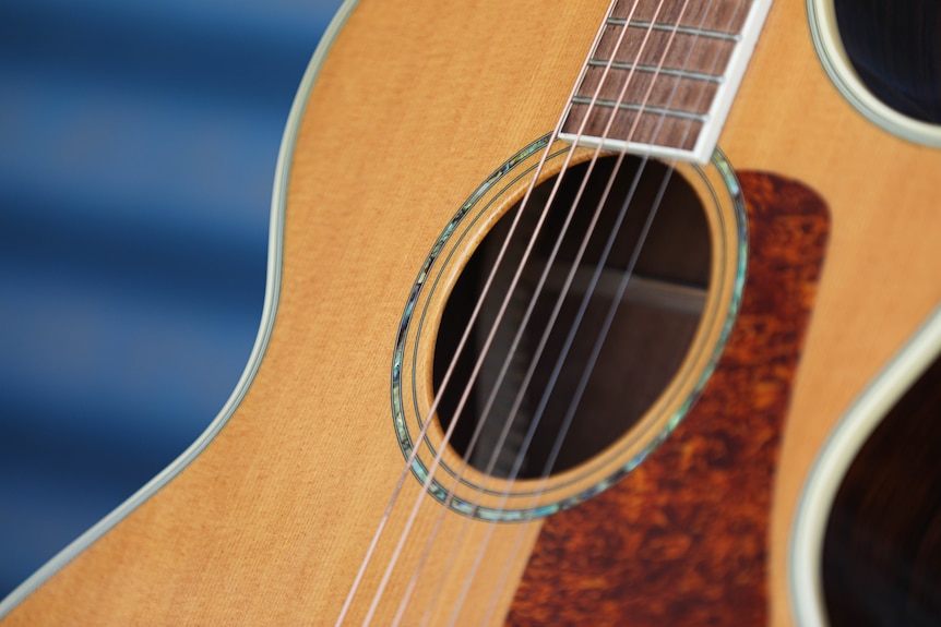 A close up of a tan guitar with a mother of pearl rosette around the sound hole.