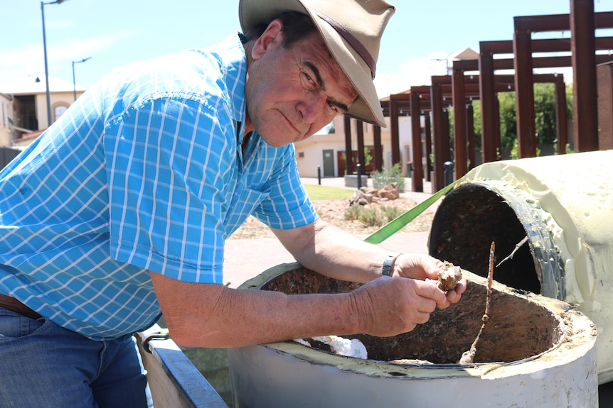 Man in a blue shirt and jeans leaning over a corroded hot water system.