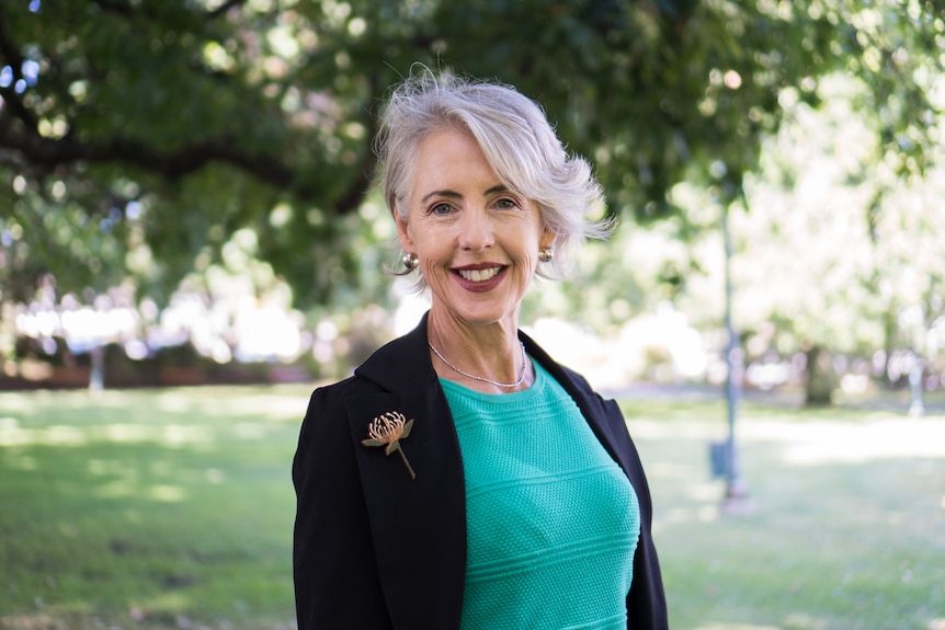 Rosalie Woodruff, wearing a green top and black blazer, smiles at the camera in a park.