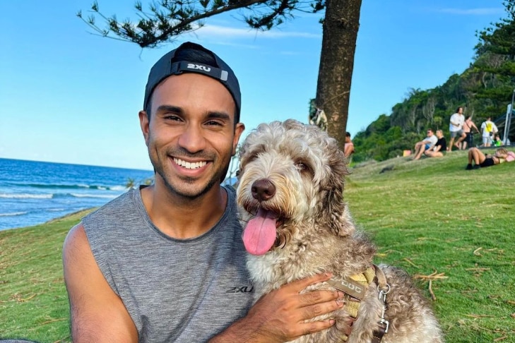 A man on a picturesque hill smiling with a dog.