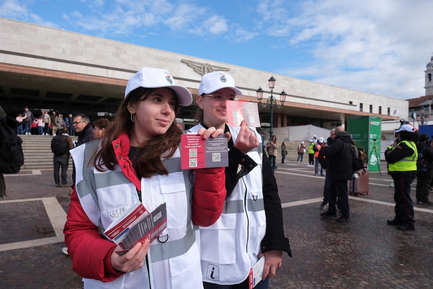 Two women stand together holding information cards.