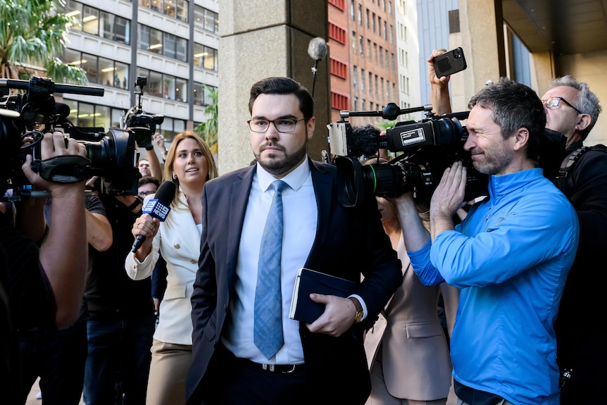 A man walks through journalists and cameras.