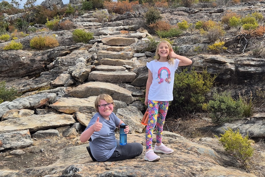 two children in bushland smile at the camera