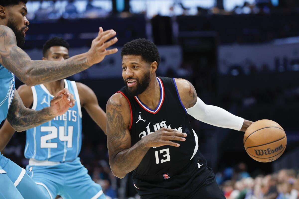 Clippers forward Paul George drives toward Charlotte Hornets center Nick Richards as forward Brandon Miller looks on.