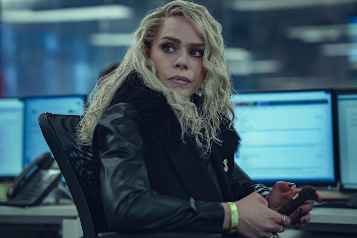 A woman in a black coat sits in an office chair turned away from her desk with her computer screen visible behind her.