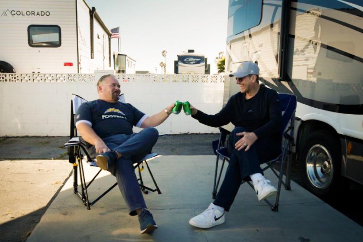 New Chargers offensive coordinator Greg Roman (left) and Jim Harbaugh give cheers with cans outside the coach's RV. 