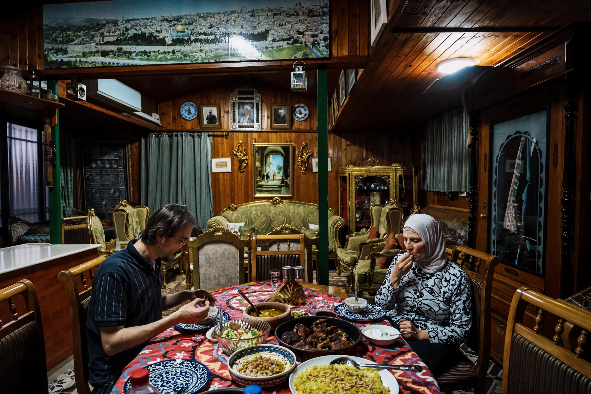 A man and older woman sit at a table in a home, eating an Iftar meal.