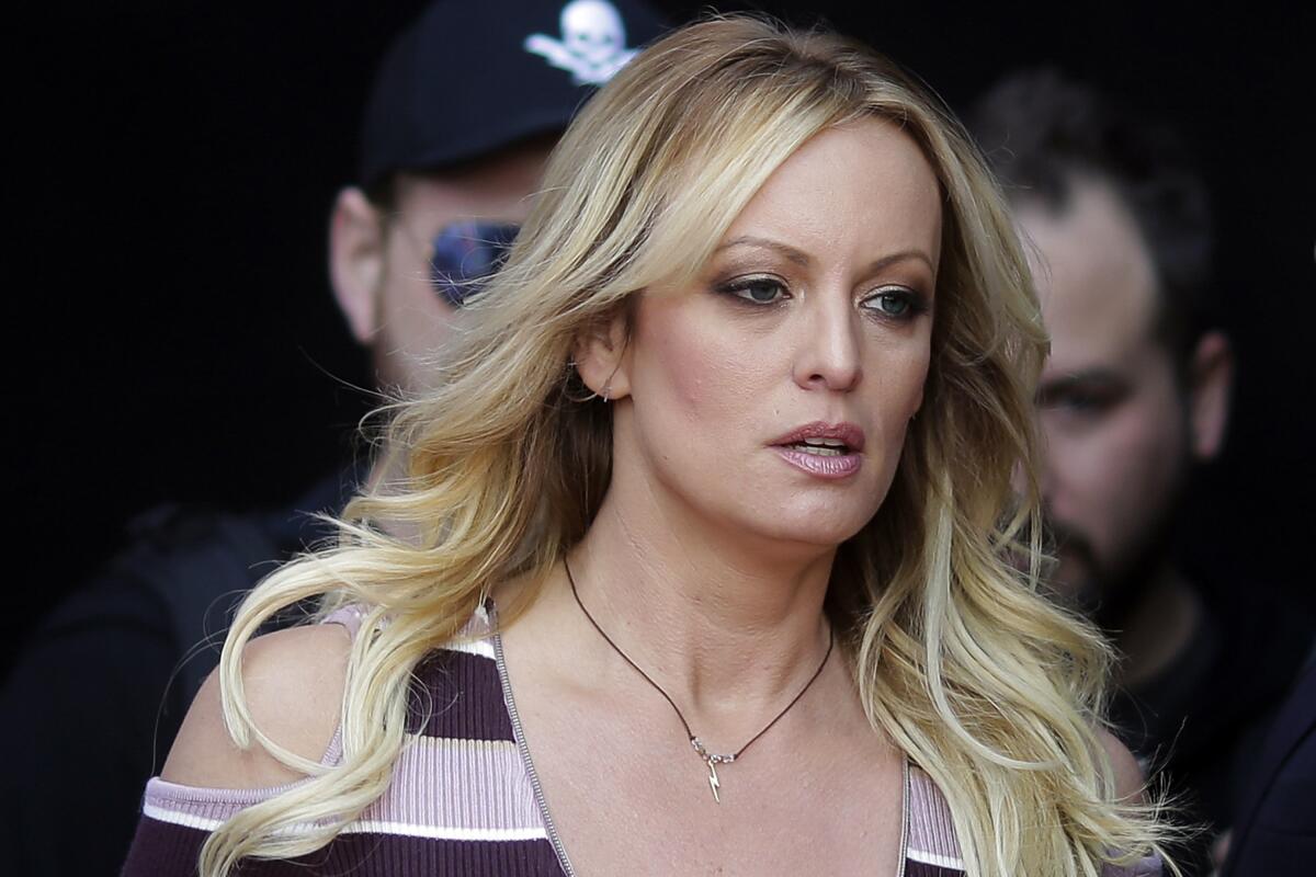 a woman with long, wavy blond hair, wearing a striped top and a necklace 