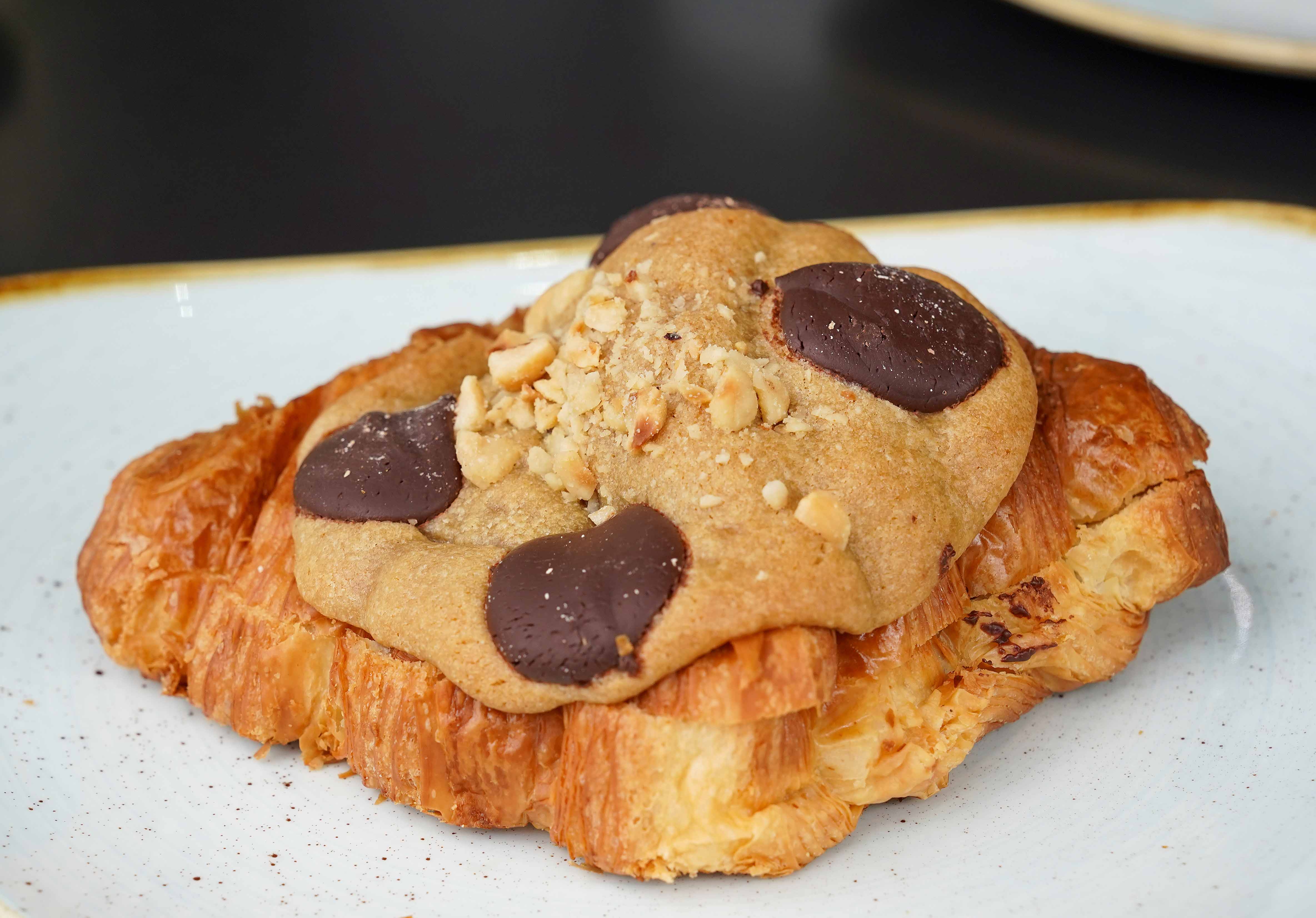 The recipe is a classic butter croissant sliced open and crammed with cookie dough, with hazelnuts sprinkled on top