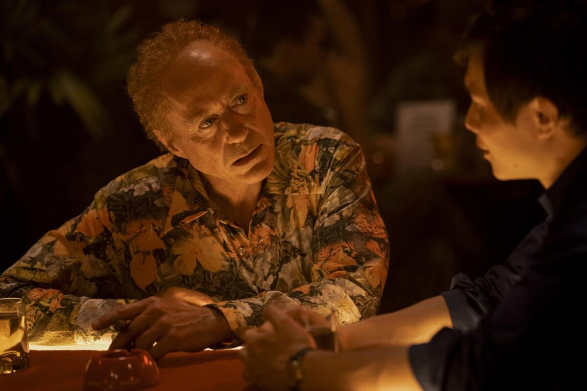 A man in a floral shirt leans against a bar.