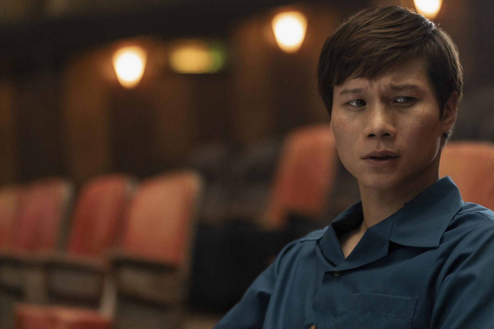 A man in a blue shirt sits in a nearly empty movie theater.