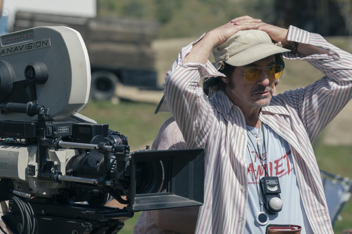 A man with his hands on his head stands next to a movie camera.