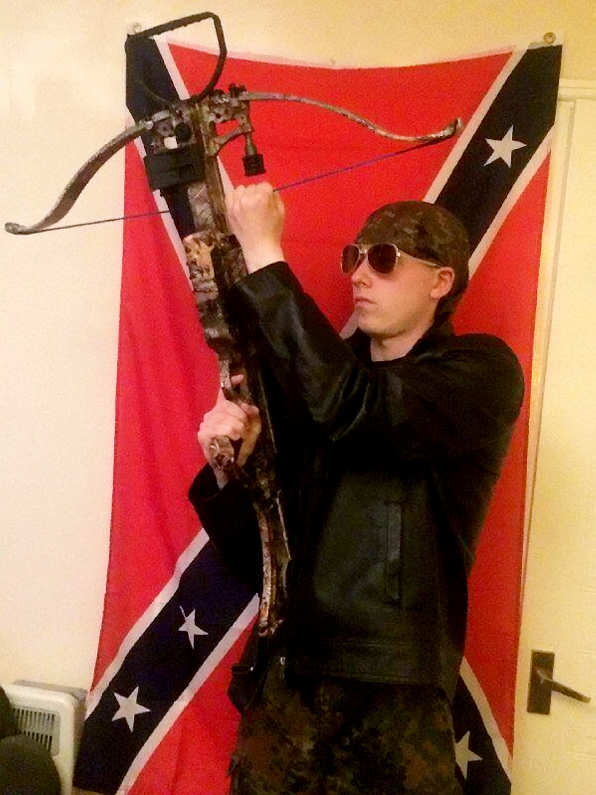 Thomas with his crossbow standing in front of a Conferderacy flag