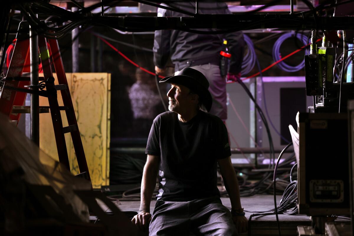 Man in black cowboy hat sits backstage surrounded by equipment.