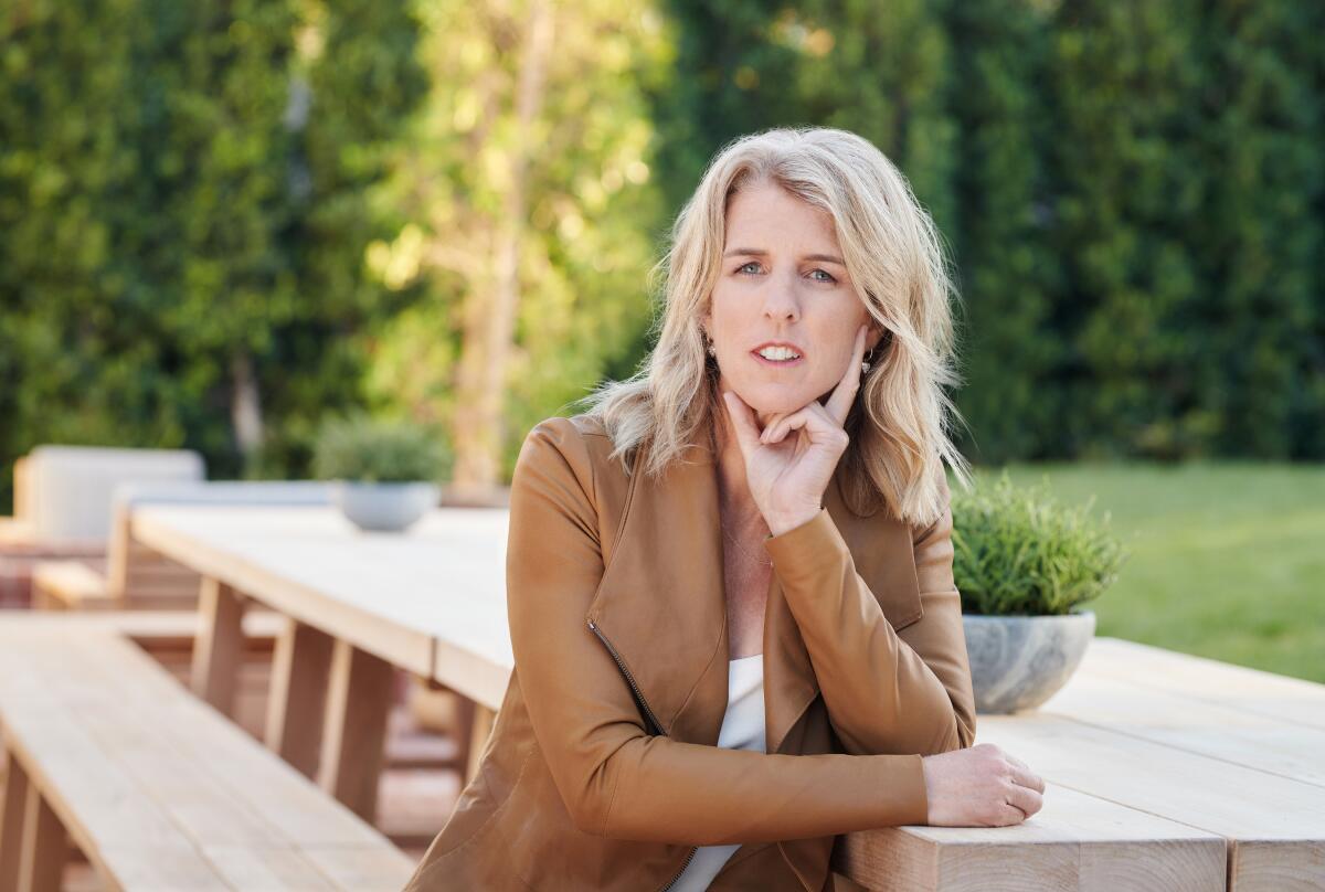 A woman in a brown jacket sits at a wooden table.