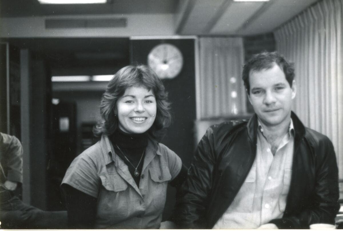 A young woman and a young man stand smiling in an office.