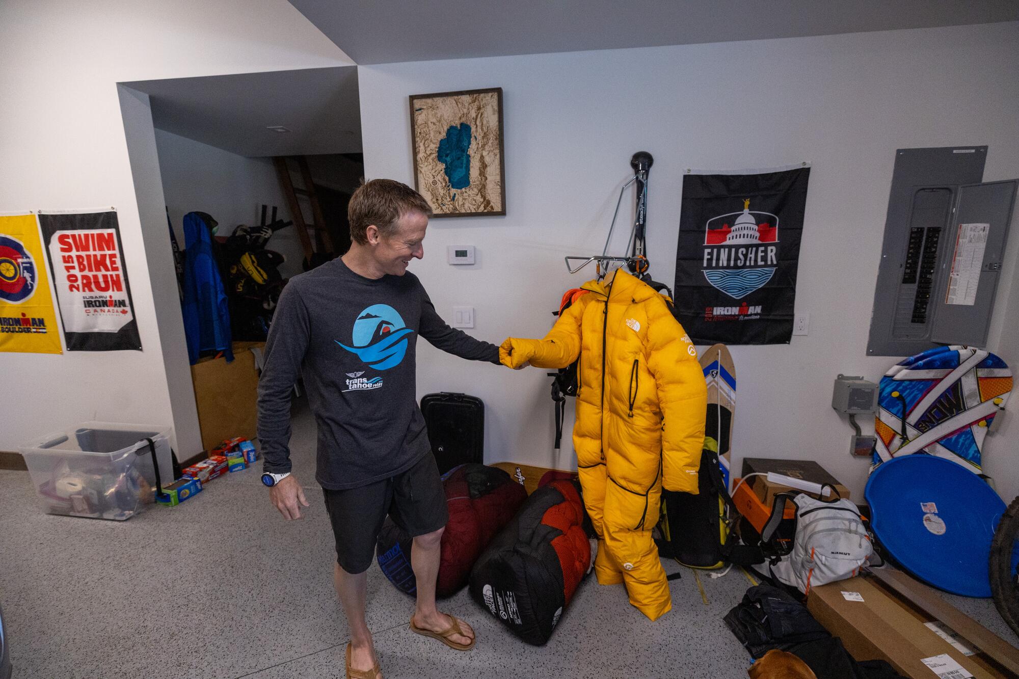 A man wearing shorts and sandals inspects a puffy yellow snowsuit.