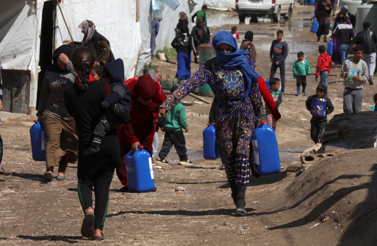 Syrian refugees walk as they carry containers at an informal tented settlement in the Bekaa valley, Lebanon March 12, 2021