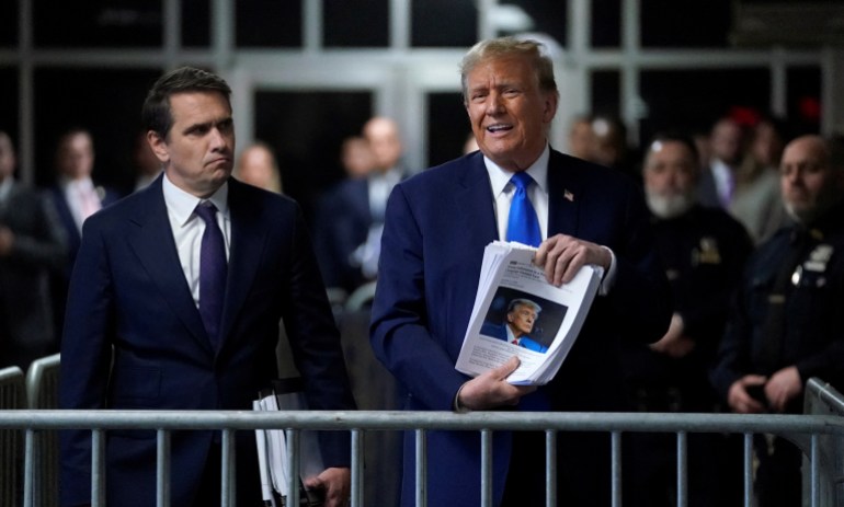 Donald Trump holds up a stack of printed articles outside a Manhattan courthouse.