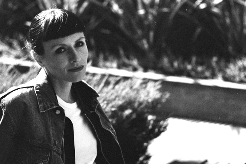 A black and white image of a woman sitting outside on a concrete ledge, slightly reclining.