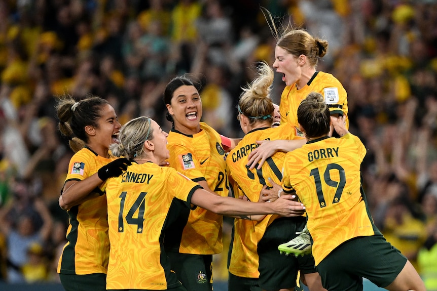 A group pf athletes in yellow shirts celebrate wildly.