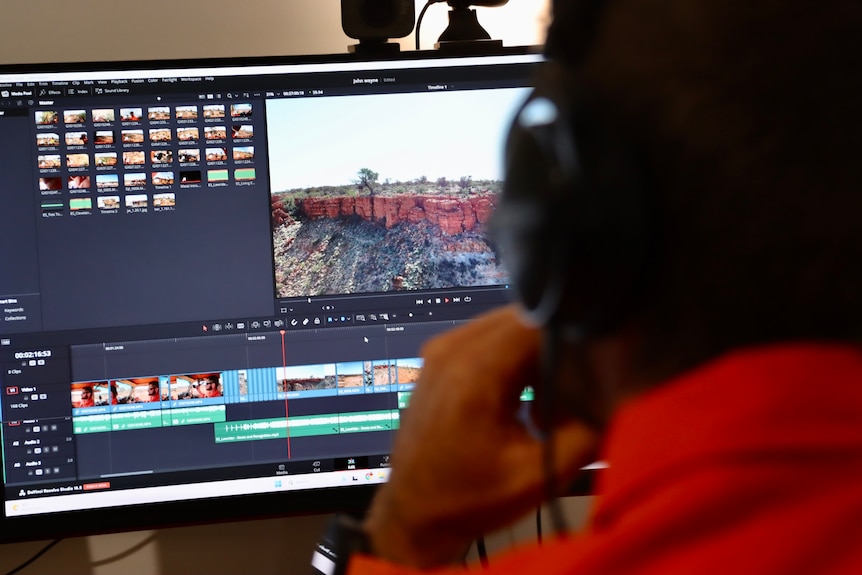 A man wearing headphones edits a video on his computer.