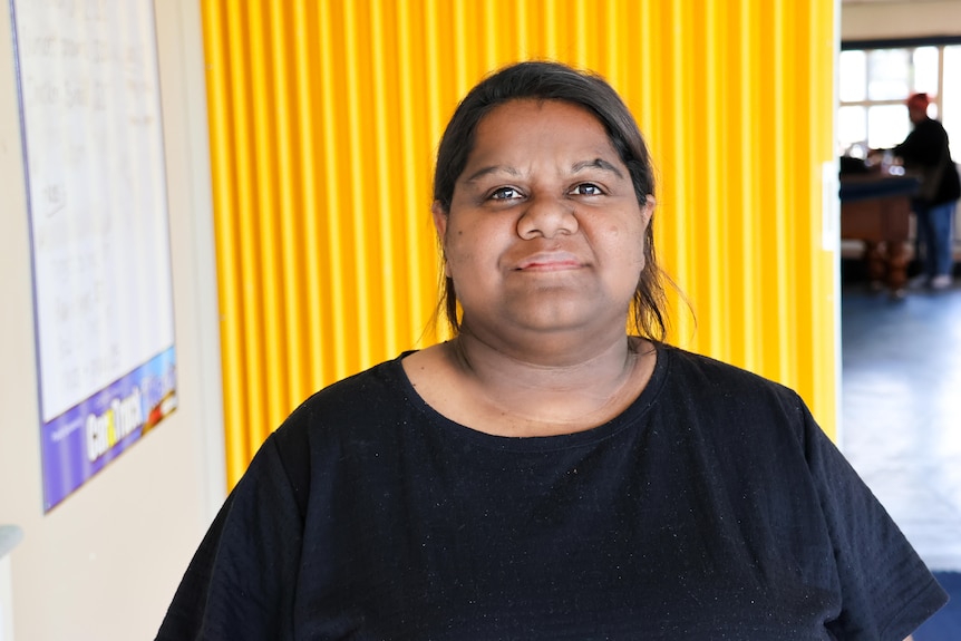 Woman in a black shirt standing in front of a yellow wall.