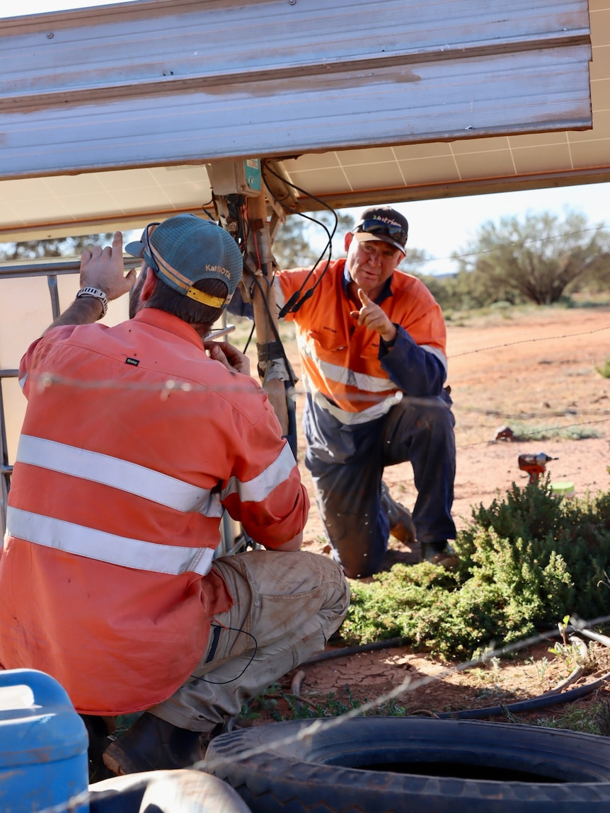 Two men wearing high-vis and hats checking disconnected cables.