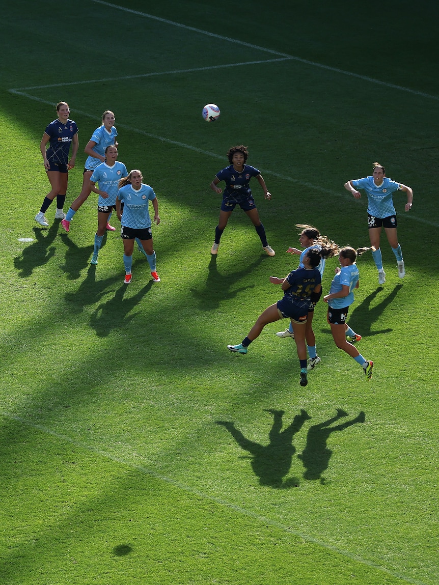 Two teams, one wearing dark blue and one wearing light blue, compete during a soccer game