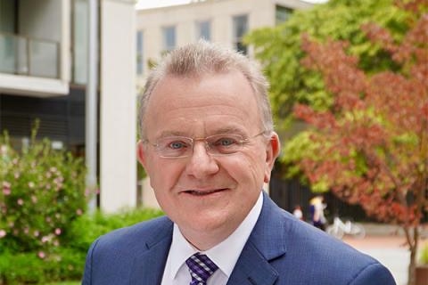 head shot of man in blue suit wearing glasses standing in a garden