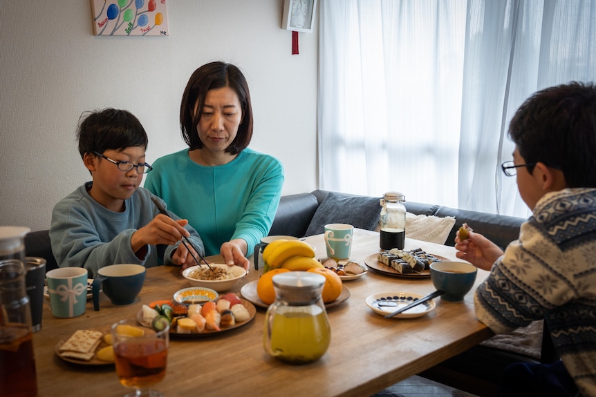 A woman and her two sons eat at a table.