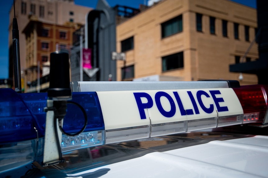 The top of a police car with the word 'Police' on it. Some city buildings are in the background