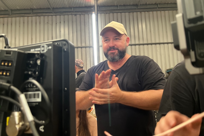 Man wearing hat with beard rubbing hands together and smiling while filming a scene for movie