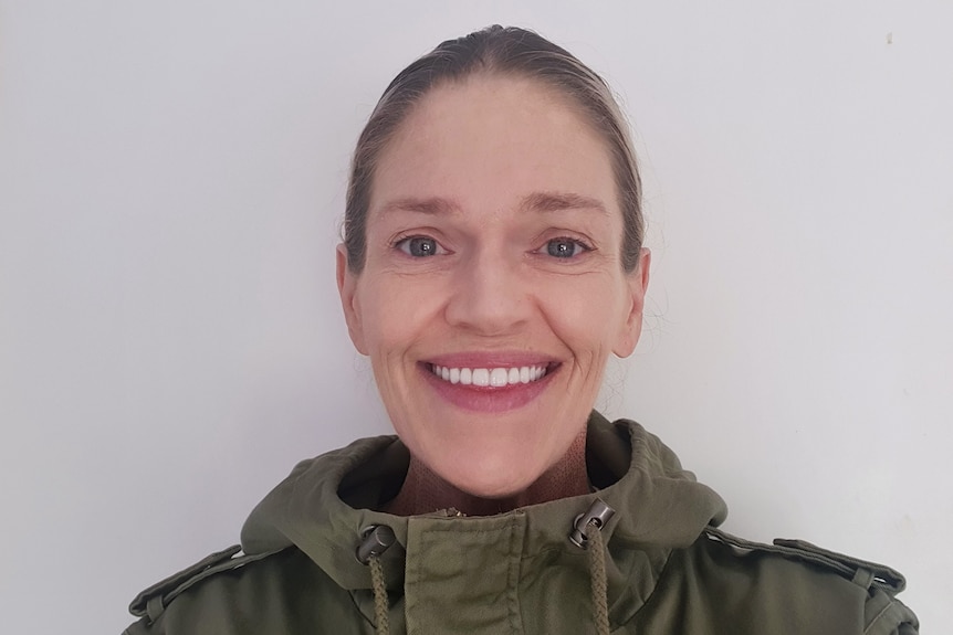 Woman, with hair pulled back, smiling and wearing khaki jacket.