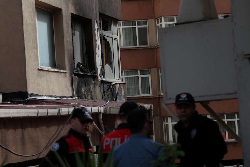 Windows on the side of a building burned and charred with glass broken. People standing outside