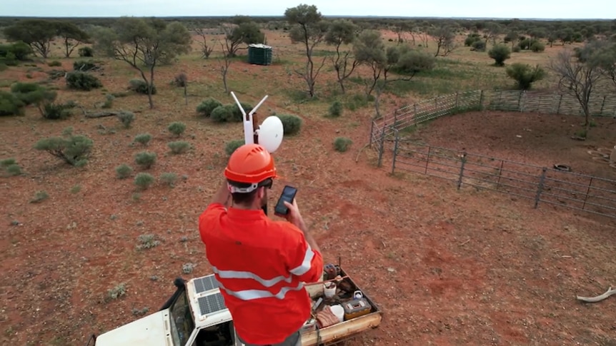 A man in hi-vis and a helmet on top of an antenna.