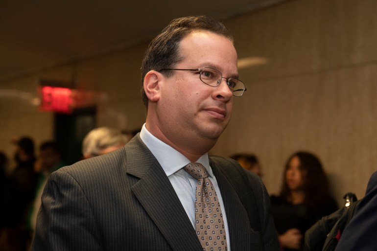 Joshua Steinglass walks through a hall in a suit and tie.