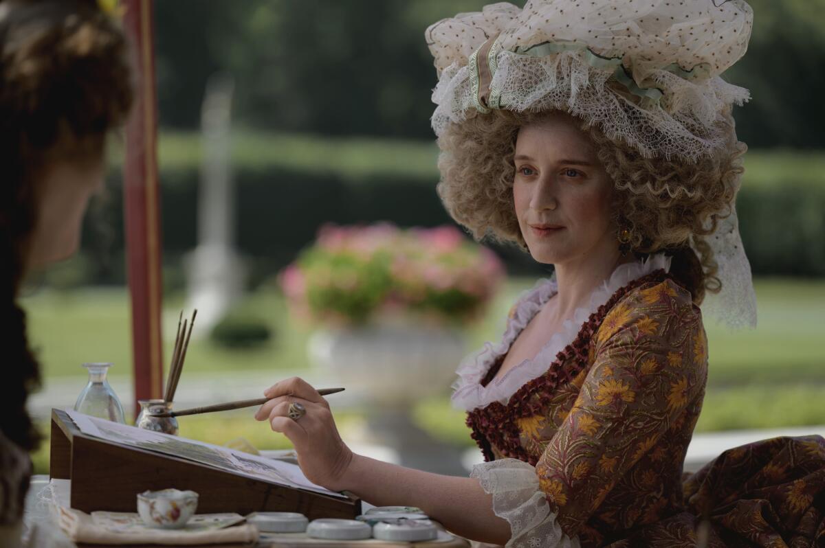 A woman in period dress holds a paintbrush in her hand.