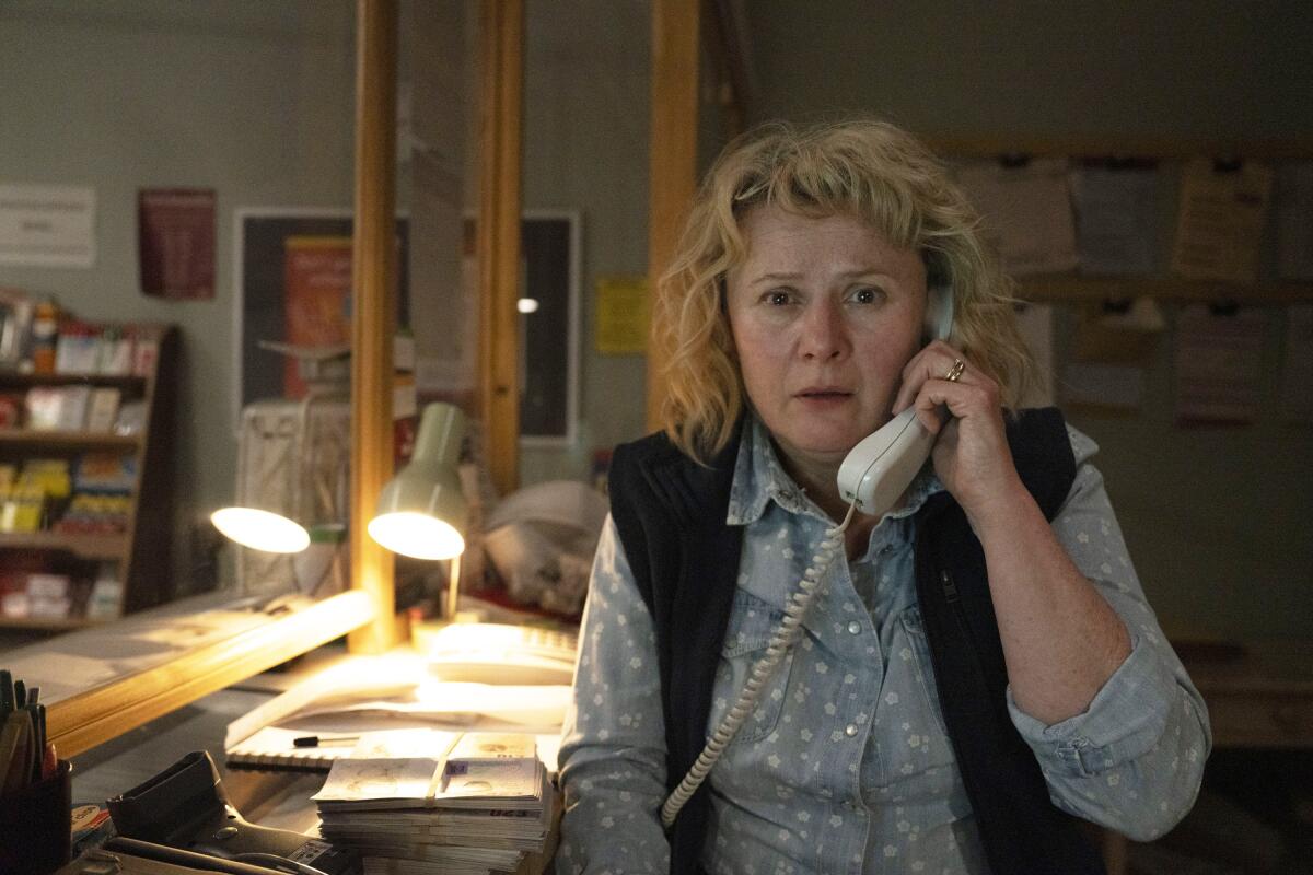 A woman sits at a desk with a corded phone to her ear.