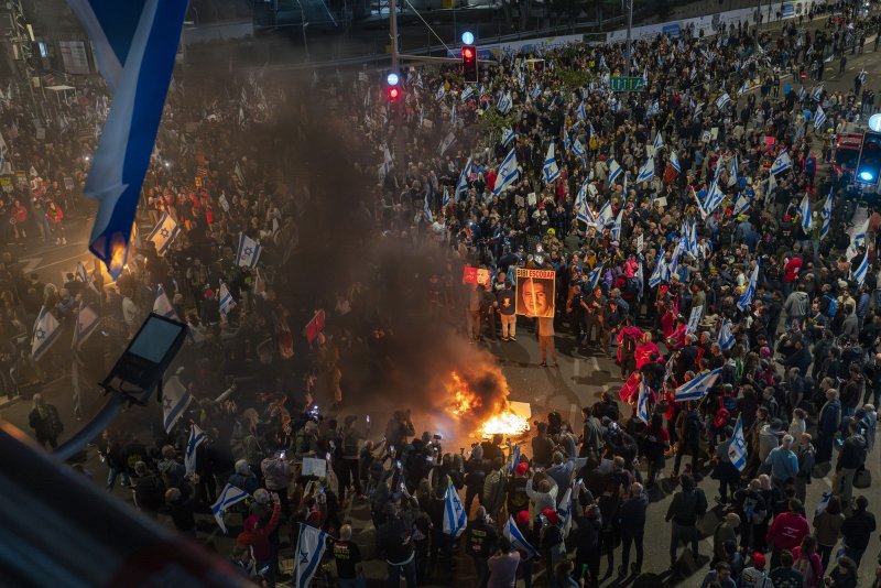 Israelis gather around a fire during a mass protest in Tel Aviv calling to oust Prime Minister Benjamin Netanyahu, to bring the hostages held by Hamas home and to peace. Organizers said 100,000 Israelis took to the streets in Tel Aviv and many other cities in Israel as the war against Hamas in the Gaza Strip enters its sixth month. Photo by Jim Hollander/UPI