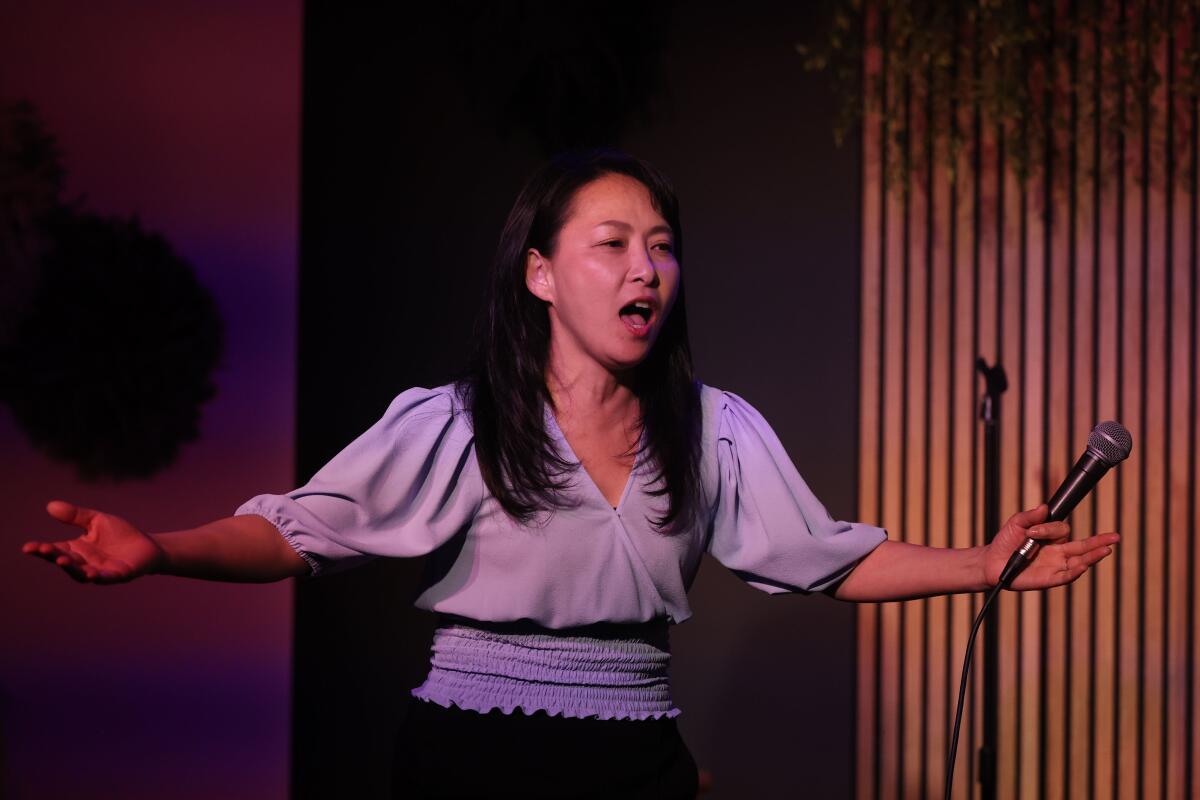 Asian female comedian on stage holding a mic