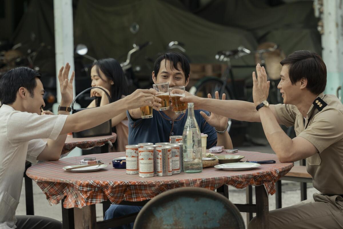 Three men at a table hold up their beers.