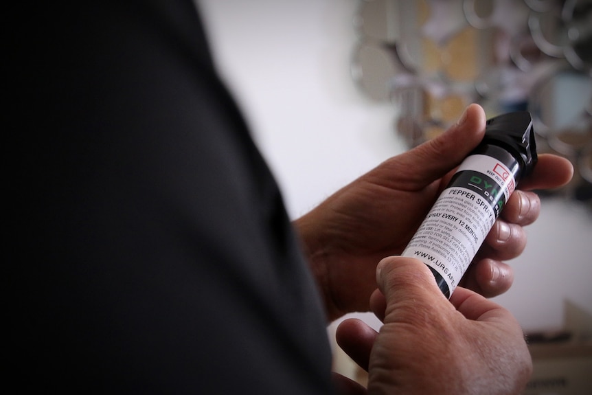 A man holding and looking at a canister or bottle labelled as "pepper spray"