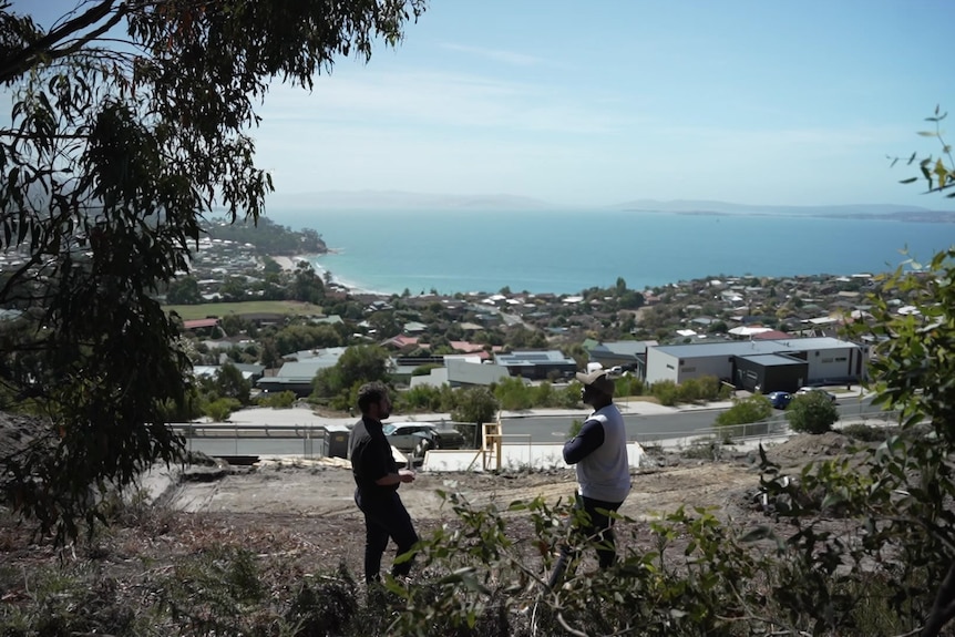 Two men stand in a site on top of a hill.