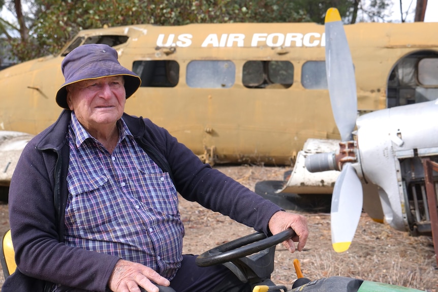 A man in a jacket and plait shirt looks off to side while a propeller and plane marked US Air Force sits in background 