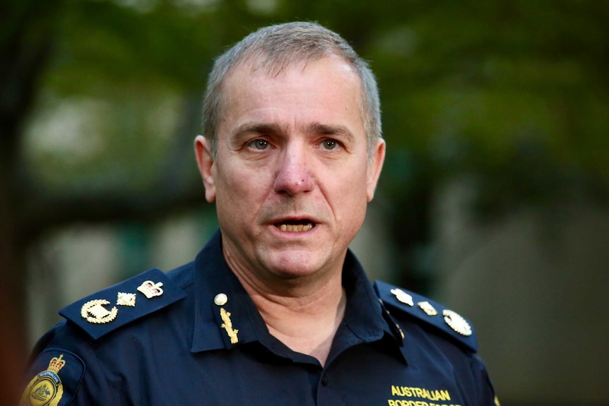 Michael Outram wears a blue police-styled uniform as he addresses the media in a courtyard