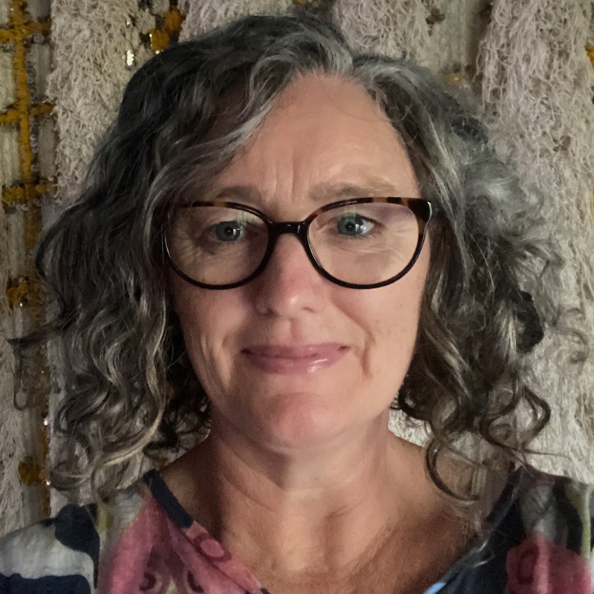 A close up shot of a woman with curly hair and glasses, smiling.