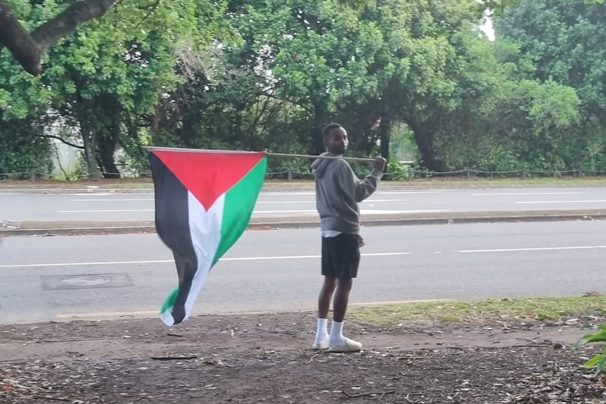 Suveen is pictured holding a pole with a palestinian flag over his shoulder.